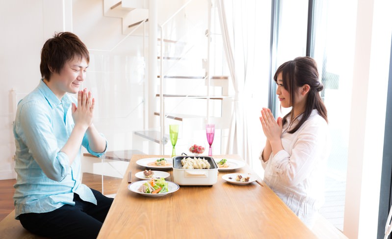 ホットプレートにのった餃子を前に、手を合わせていただきますをしている男女のカップルの写真