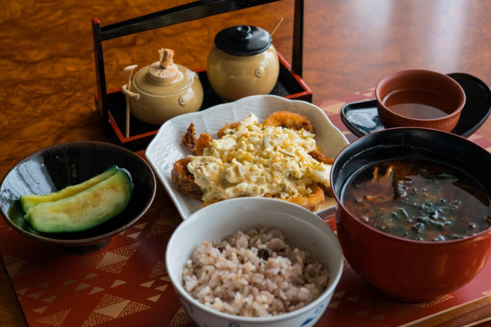 お味噌汁、五穀米ご飯、タルタルソースののったフライ、なすびのつけものの食事