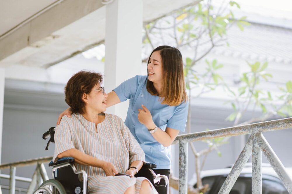 車いすに乗った女性の肩に手をかけながら微笑む介護士の女性