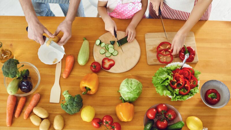 キッチンで野菜を切って3人で調理している写真